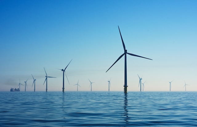 Wind Turbines sit offshore the coast of the UK in the sunset. These will produce huge amounts of power for cities.