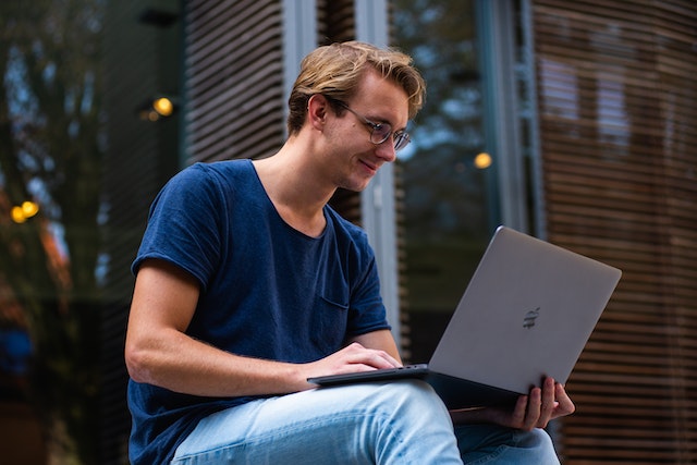 A man sitting outside on his laptop researching the qualifications he needs to become an electrician.