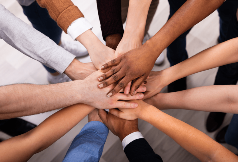 Several electricians' hands in a circle, stacked on top of each other all of whom are from different ethnic backgrounds encouraging equality and diversity in the electrical industry.